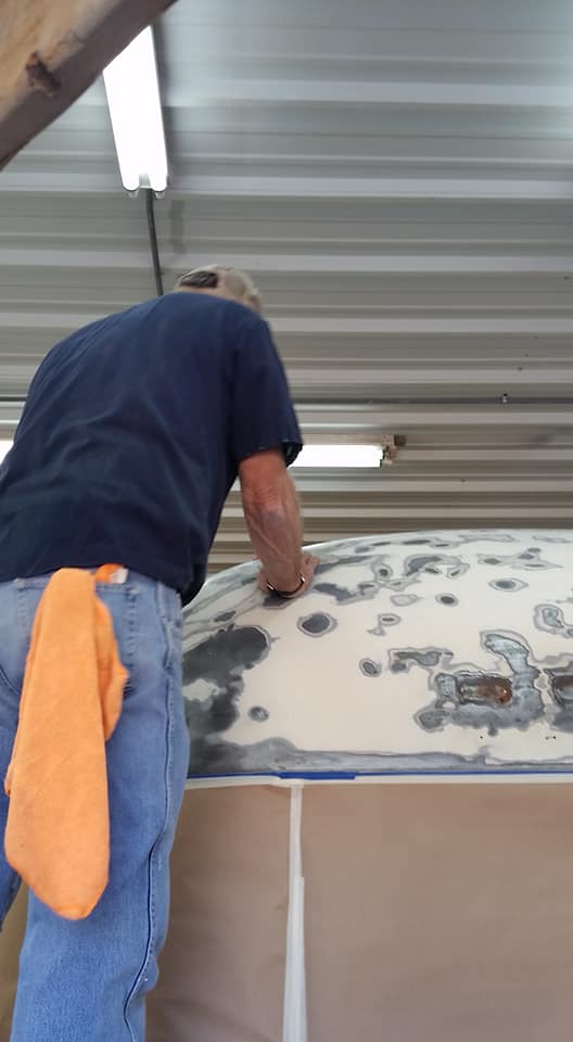 The interior of an Airstream trailer undergoing a remodel, with the walls stripped down to the aluminum skin covered in insulation, electrical wires exposed, and a ladder in the center.